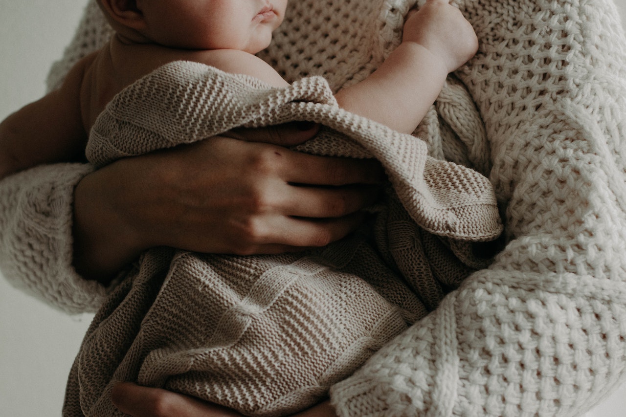 Eine Mutter, die ihr Baby im Arm hält umhüllt von einer naturfarbenen Decke